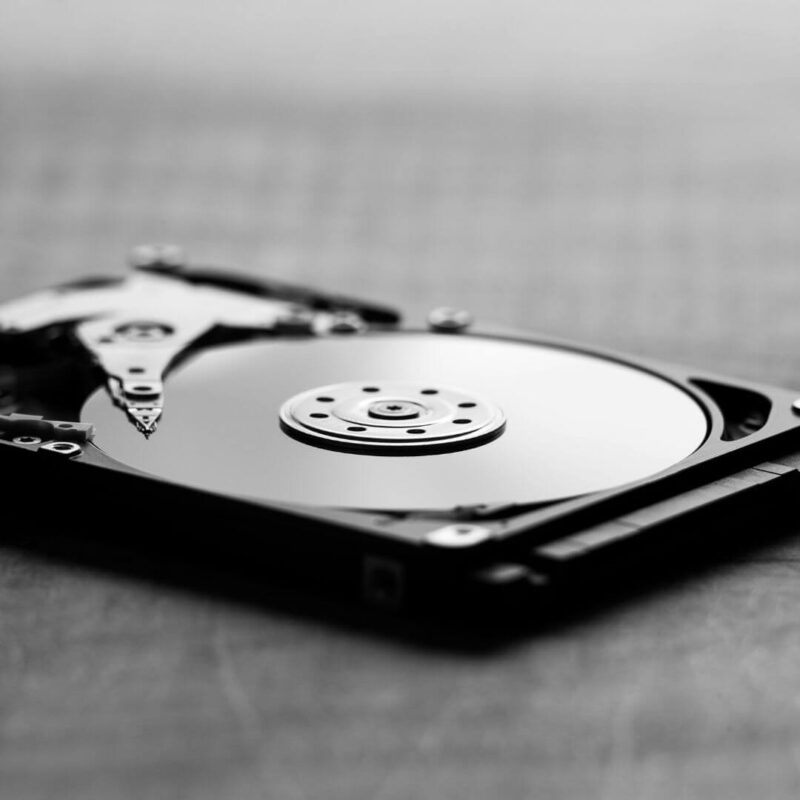 Close-up of an open hard disk drive showing exposed platters and read-write arm, placed on a reflective surface.