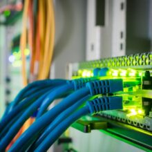 Close-up of a network switch with multiple blue Ethernet cables connected, illuminated by green indicator lights.