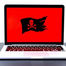 A laptop screen displays a red background with a black pirate flag featuring a skull and crossbones, indicating a potential cyber threat or malware.
